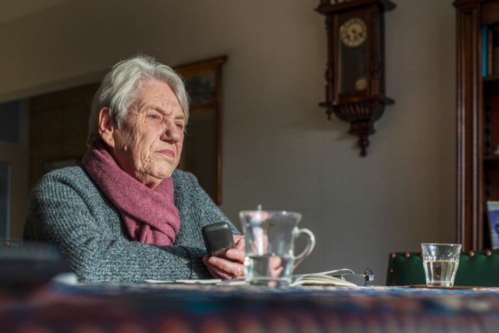 een oudere vrouw zit aan tafel in gedachten verzonken